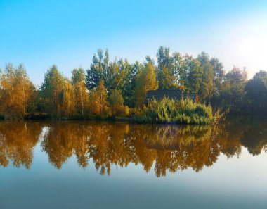 Sonbaharda yansımasıyla gölün kıyısında küçük bir ev..