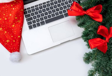Beyaz arka planda Noel Baba şapkası ve Noel Ağacı olan dizüstü bilgisayar, üst manzara, boşluğu kopyala.