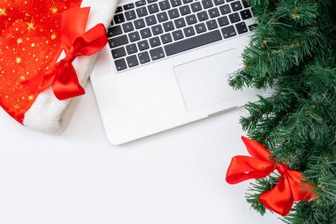Beyaz arka planda Noel Baba şapkası ve Noel Ağacı olan dizüstü bilgisayar, üst manzara, boşluğu kopyala.