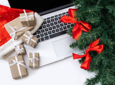 Hediyeli dizüstü bilgisayar, kırmızı şapka, Noel ağacı ve beyaz arka planda paketleme kutuları, üst görünüm, dağıtım konsepti.