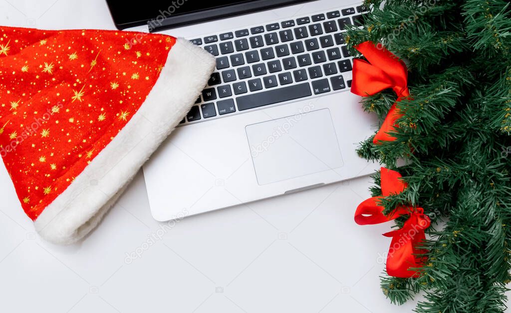Laptop with hat of Santa Claus and Christmas Tree on the white background, top view, copy space.