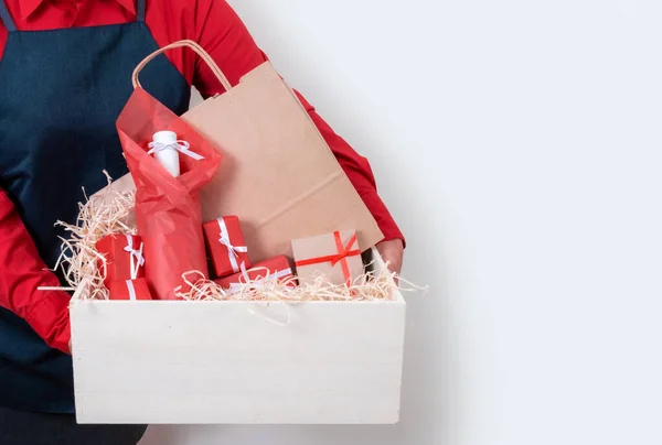 Hands of Deliver in red shirt and apron hold Gifts, Packing boxes and bottle of wine on the white background, delivery concept.