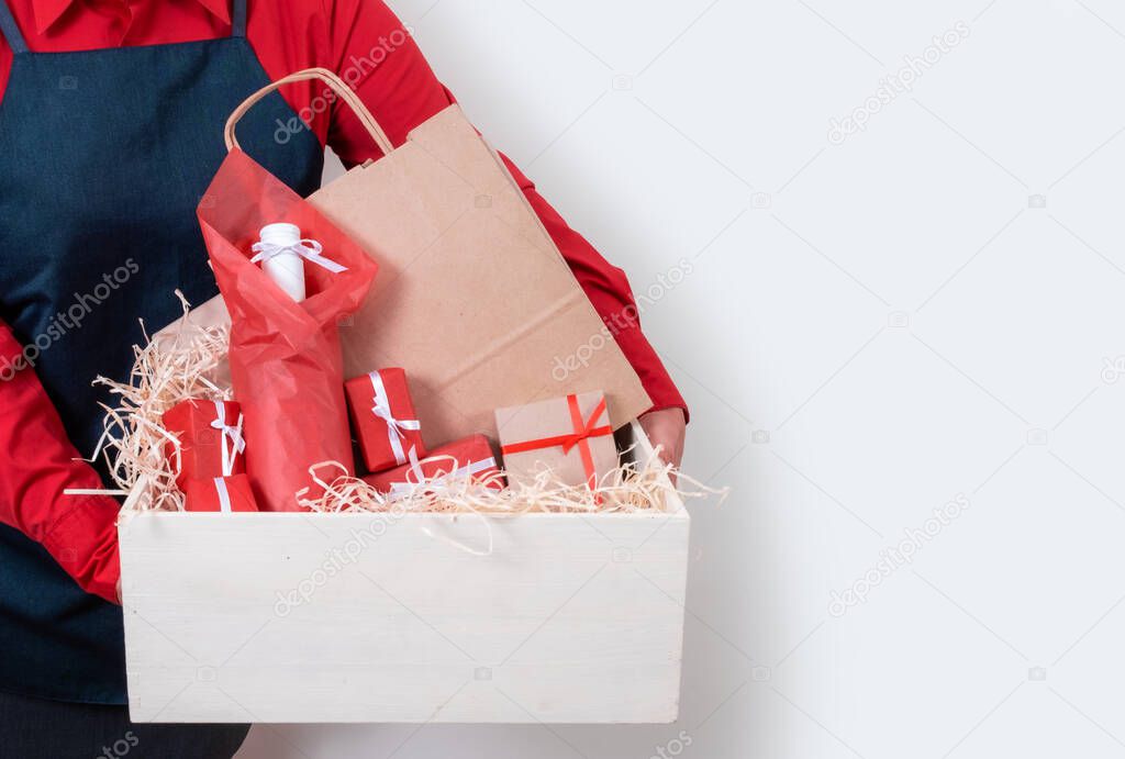 Hands of Deliver in red shirt and apron hold Gifts, Packing boxes and bottle of wine on the white background, delivery concept.
