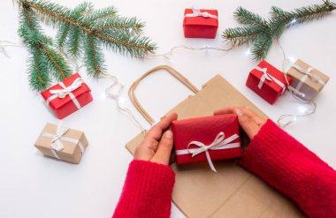 Torba, kutu ve yılbaşı ağacıyla dolu bir arka planda hediye kutusunu tutan eller.