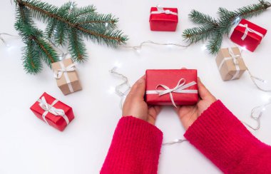 Torba, kutu ve yılbaşı ağacıyla dolu bir arka planda hediye kutusunu tutan eller.
