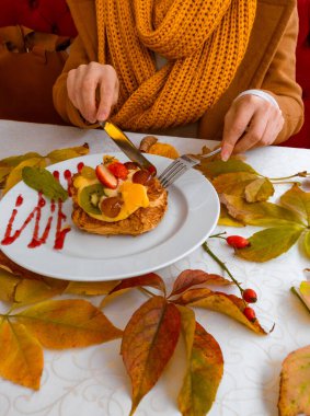 Sonbahar yaprakları üzerinde meyveli kek olan beyaz tabağı tutan kadın eller..