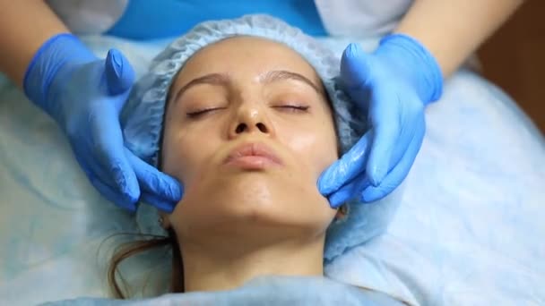 Una ragazza giovane e bella al ricevimento di un cosmetologo. Cosmetologo rende una donna procedure ringiovanenti sulla pelle del viso — Video Stock