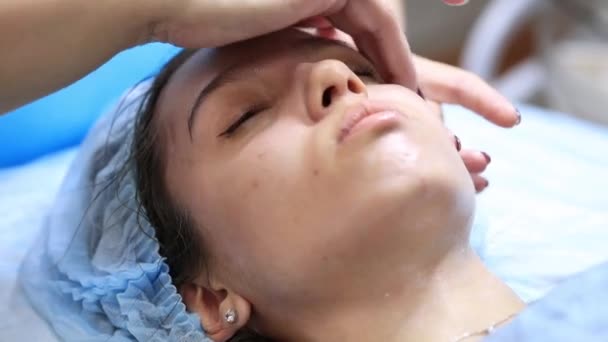 Una chica joven y hermosa en la recepción de un cosmetólogo. Cosmetólogo hace una mujer procedimientos rejuvenecedores en la piel de la cara — Vídeos de Stock