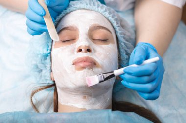 Kozmetikçiyle doktor randevusunda olan genç bir kadın. Güzel bir kız yüzüne canlandırıcı bir maske takıyor.