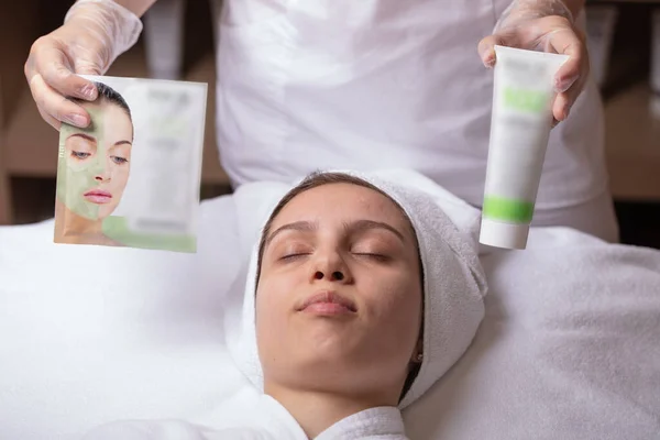 A young woman is given a rejuvenating mask of green algae on her face