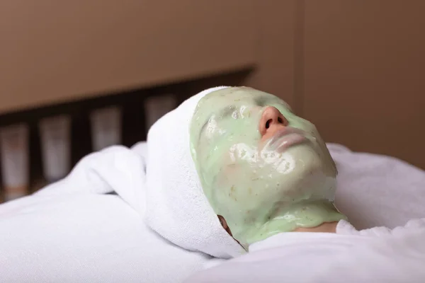 A young woman is given a rejuvenating mask of green algae on her face