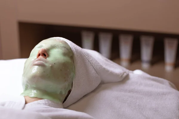 A young woman is given a rejuvenating mask of green algae on her face