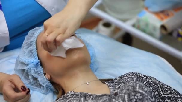 En ung och vacker flicka vid en kosmetologmottagning. Kosmetolog gör en kvinna föryngrande förfaranden på huden i ansiktet — Stockvideo
