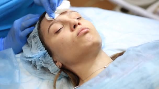 Una ragazza giovane e bella al ricevimento di un cosmetologo. Cosmetologo rende una donna procedure ringiovanenti sulla pelle del viso — Video Stock