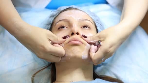 Een jong en mooi meisje op de receptie van een cosmetoloog. Cosmetoloog maakt een vrouw verjongende procedures op de huid van het gezicht — Stockvideo