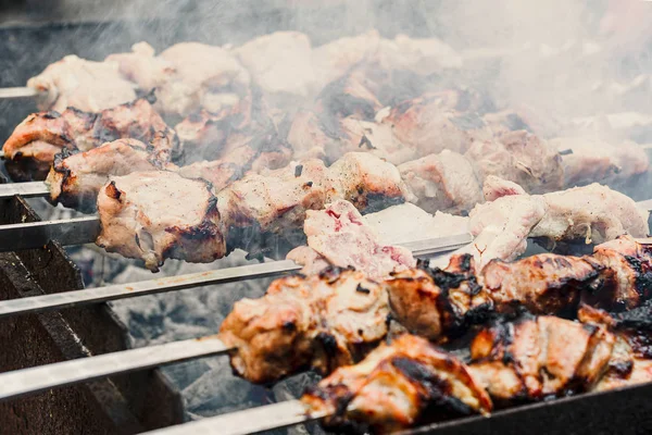 Close up shot of appetizing hot shish kebab on metal skewers prepares on the coals outdoors. Grilling shashlik on barbecue grill. — Stock Photo, Image