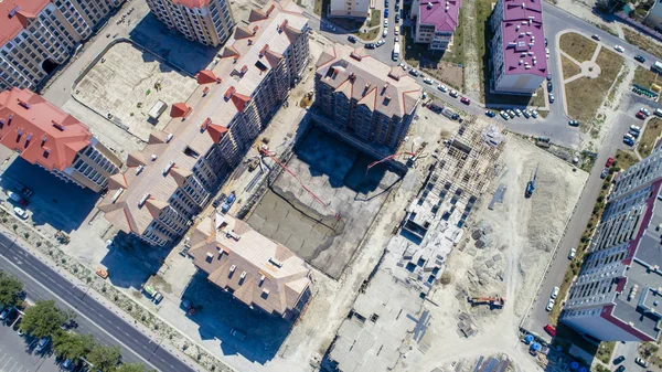 the casting of the concrete Foundation of a house. Bird\'s-eye view. Two concrete pumps feed the solution into an earthen pit, where workers level the concrete. Concrete is transported in a concrete mixer. Around are already built multi-storey houses