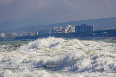Karadeniz 'de güçlü ve tehlikeli bir fırtına. Gelendzhik, sahil ve deniz feneri beldesinin arka planda Gelendzhik Körfezi 'nde güzel ve büyük fırtına dalgası. Arka planda, oteller, gezinti yeri ve dağlar.