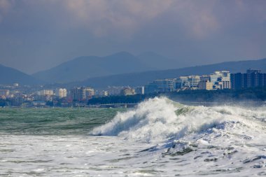 Karadeniz 'de güçlü ve tehlikeli bir fırtına. Gelendzhik, sahil ve deniz feneri beldesinin arka planda Gelendzhik Körfezi 'nde güzel ve büyük fırtına dalgası. Arka planda, oteller, gezinti yeri ve dağlar.