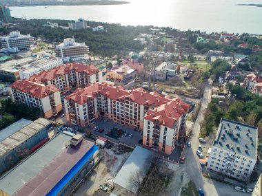 Kırmızı çatılı iki çok katlı apartman dairesi. Kuş bakışı görüş. Deniz koyunun kıyısındaki dağların eteklerinde yer alıyor.