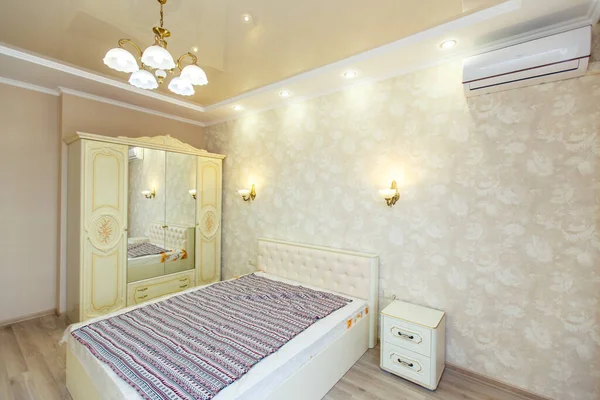 Kamer in felle kleuren met een nieuwe renovatie. Een groot wit bed, een witte kledingkast en een nachtkastje ernaast. Lampen op de muren — Stockfoto