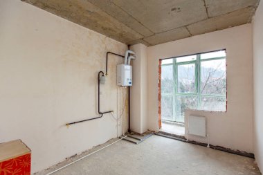 Henüz bitmemiş küçük bir oda. Yenilenmemiş odalar. Yeni bina. Duvarlar sıvanmış, yerler betonla kaplanmış. Bir atama var.