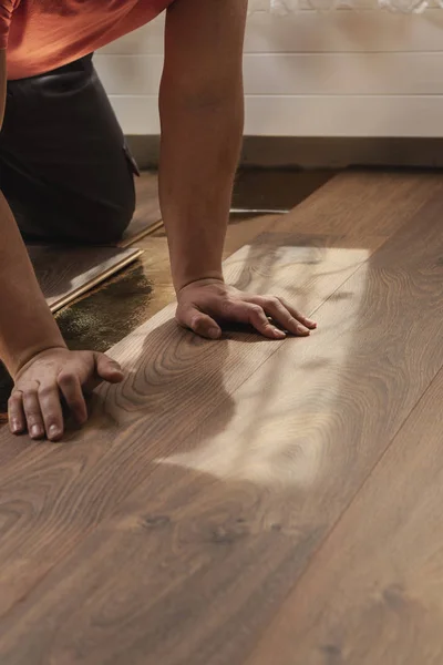 Manos del trabajador presionando los tablones mientras que pone piso laminado — Foto de Stock