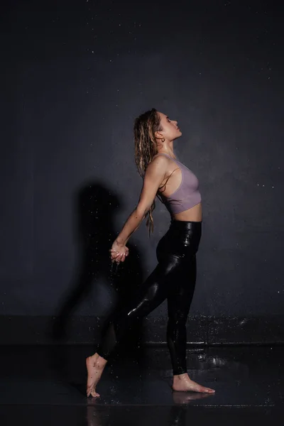 beautiful young girl in top and shorts doing yoga pose under the drops of water