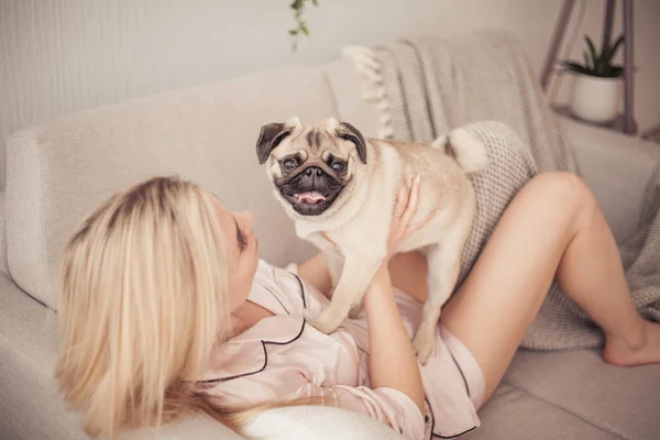 Lovely girl hugging her pug and playing with him in the house