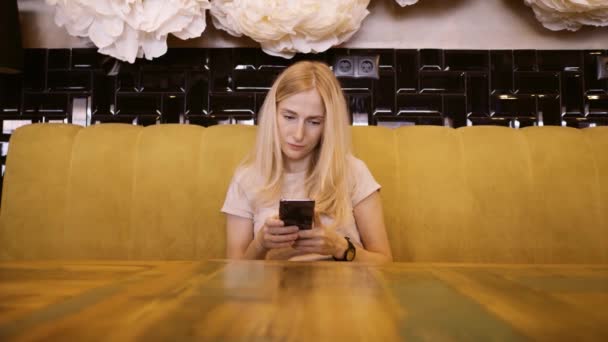 Μπροστινή άποψη του όμορφη νεαρή γυναίκα χρησιμοποιώντας το κινητό της τηλέφωνο στο café. Γυναίκα με τη χρήση του app στο smartphone στο καφενείο να περιμένει για γεύμα και γραπτών μηνυμάτων στο κινητό τηλέφωνο — Αρχείο Βίντεο