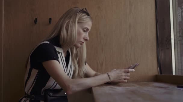 Portrait de jeune femme séduisante utilisant un téléphone intelligent et vérifiant les réseaux sociaux. Café intérieur près de la fenêtre — Video