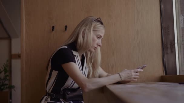 Porträtt av attraktiv ung kvinna med hjälp av smartphone och kontrollera sociala nätverk. Inside café nära fönster — Stockvideo