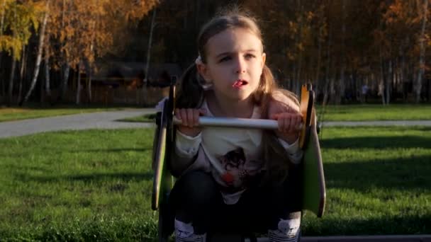 Pequeña niña dulce swing y jugar en el patio de recreo en el parque — Vídeo de stock