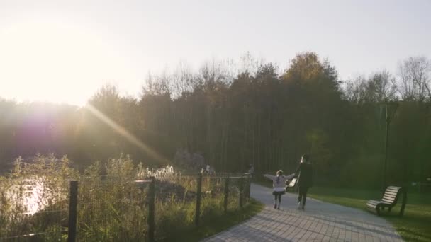 A mãe caminha com a filha no parque ao pôr-do-sol. Fugas de luz. Tempo de outono. Criança e pai em um parque de verão ao pôr do sol . — Vídeo de Stock