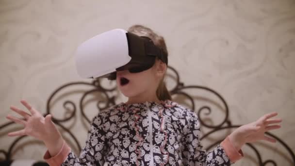 Little girl in VR headset looking up and trying to touch objects in virtual reality at home indoors. — 图库视频影像
