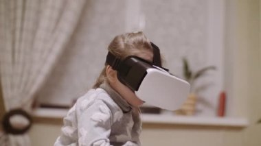 Yukarıya bakıyor ve sanal gerçeklik evde kapalı nesneleri dokunmak çalışırken Vr kulaklık, küçük kız.