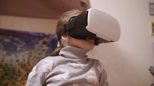Menina no fone de ouvido VR olhando para cima e tentando tocar objetos em realidade virtual em casa dentro de casa . — Vídeo de Stock