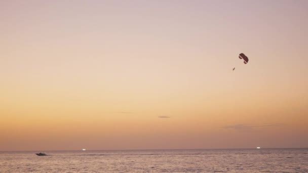 Actividad de paracaídas 0 en la playa tropical después del atardecer, tiro de barco remolcando paracaídas con la gente. Aguas tranquilas del mar y hermoso cielo aseado en el fondo — Vídeo de stock