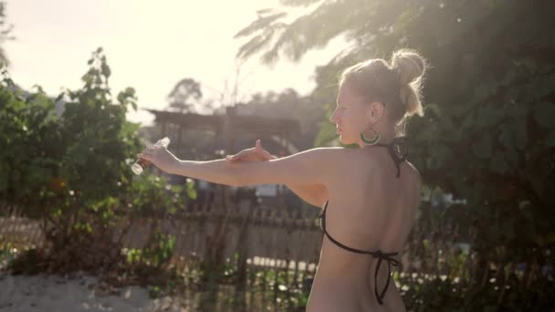 Aceites corporales femeninos. Mujer joven en bikini cremas de su cuerpo. Fondo de árbol verde — Vídeos de Stock