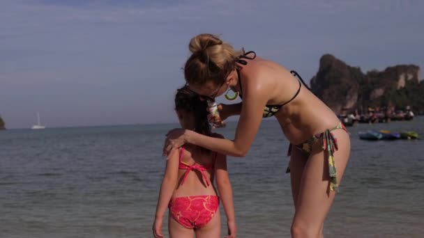 Mother smears little daughter back with sunscreen. — Stock Video