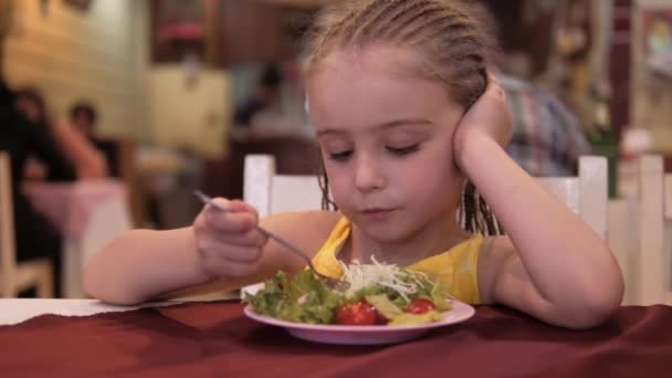 小さな女の子はレストランで食欲を持ってグリーンサラダを食べます。良い健康の概念 — ストック動画