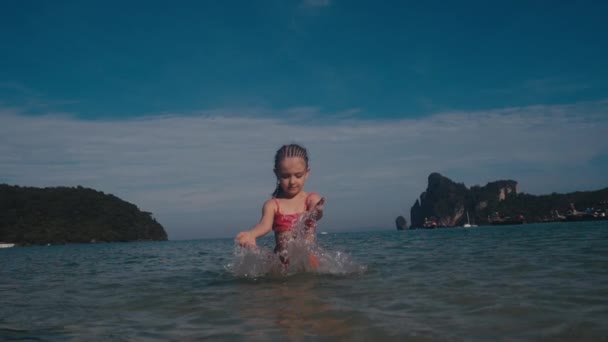 Kleines schönes Mädchen im Badeanzug spielt im warmen Sommermeer. Wasserspritzer, — Stockvideo