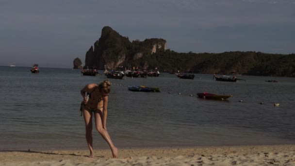 Mujer rubia bronceada bastante joven en bikini en la playa de arena. Mantener su cuerpo con aceite bronceador . — Vídeos de Stock
