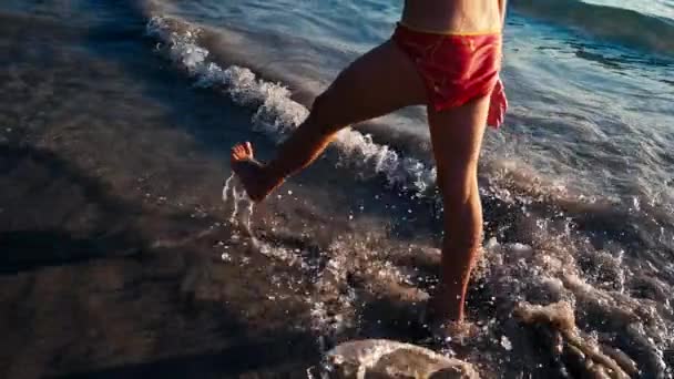 Movimento lento de uma menina descalça correndo na areia molhada ao longo do mar na luz quente do sol da noite. Infância descuidada e feliz — Vídeo de Stock