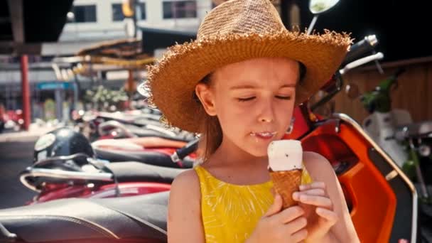 Κοριτσάκι σε ψάθινο καπέλο που τρώει παγωτό υπαίθρια Street. Πορτρέτο του καλοκαιριού — Αρχείο Βίντεο