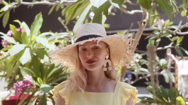 Porträt einer schönen jungen Frau mit Strohhut an einem sonnigen Tag, die in die Kamera blickt — Stockvideo