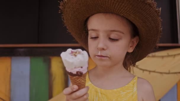 Little girl in straw hat eating ice-cream outdoors Street. Summer portrait — Stock Video