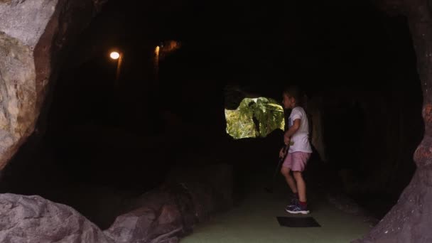 Infancia juguetona. Pequeña niña jugar mini golf al aire libre — Vídeos de Stock