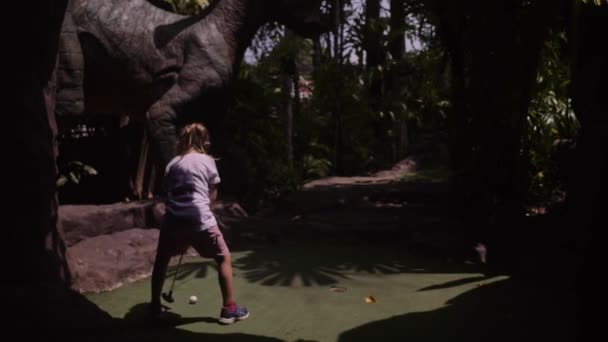 Infancia juguetona. Pequeña niña jugar mini golf al aire libre — Vídeo de stock