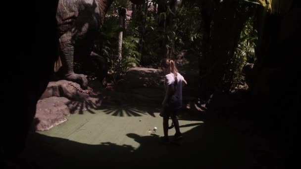 Игривое детство. Маленькая девочка играет в мини гольф под открытым небом — стоковое видео